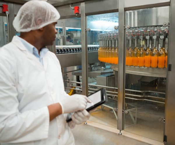 Male worker holding digital tablet while inspecting juice bottles in factory